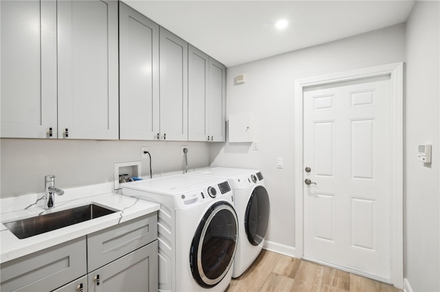 clothes washing area with cabinets, light hardwood / wood-style flooring, washer and dryer, and sink