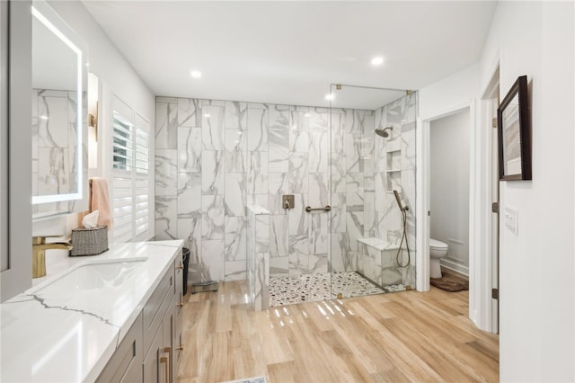 bathroom featuring hardwood / wood-style flooring, vanity, toilet, and tiled shower