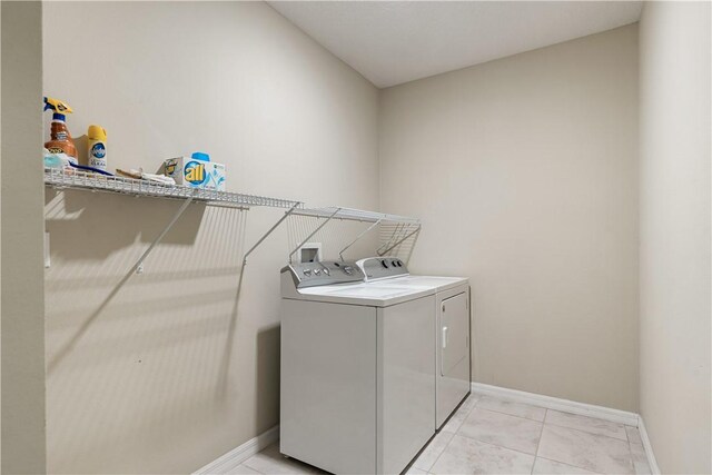 clothes washing area featuring washer and clothes dryer, laundry area, baseboards, and light tile patterned flooring