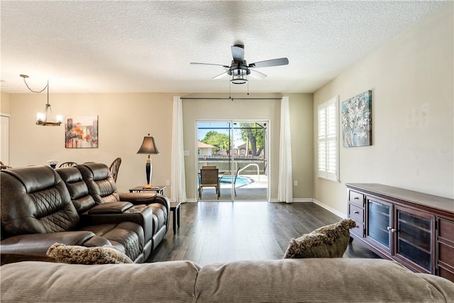 living room with dark wood-style floors, ceiling fan with notable chandelier, a textured ceiling, and baseboards