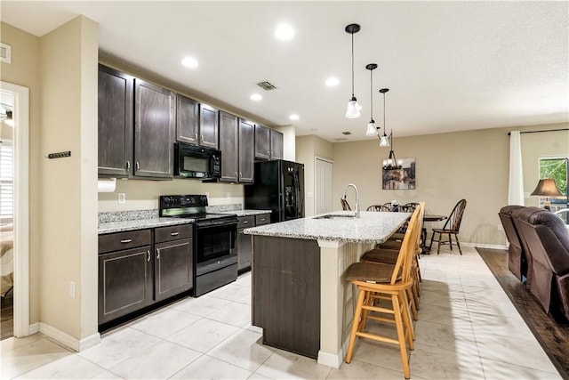 kitchen featuring visible vents, black appliances, a sink, open floor plan, and a breakfast bar area