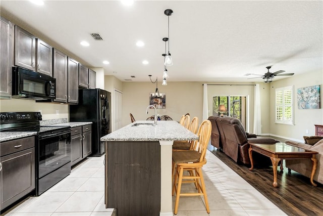 kitchen with visible vents, black appliances, a sink, a kitchen breakfast bar, and open floor plan