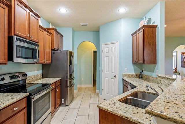 kitchen featuring stainless steel appliances, a sink, arched walkways, visible vents, and light stone counters