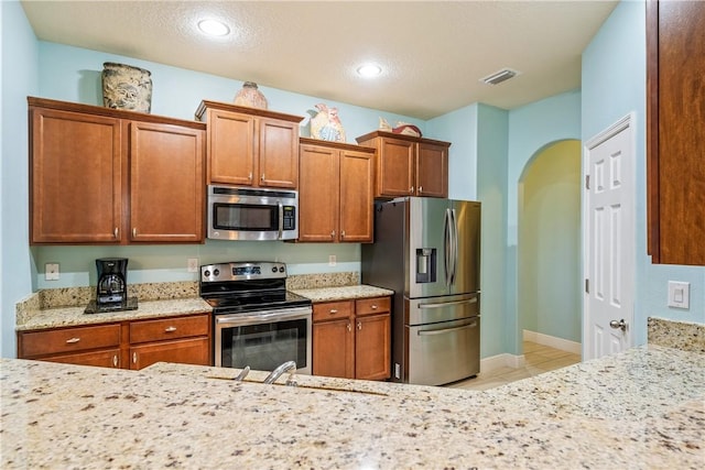 kitchen featuring brown cabinets, arched walkways, appliances with stainless steel finishes, and light tile patterned flooring