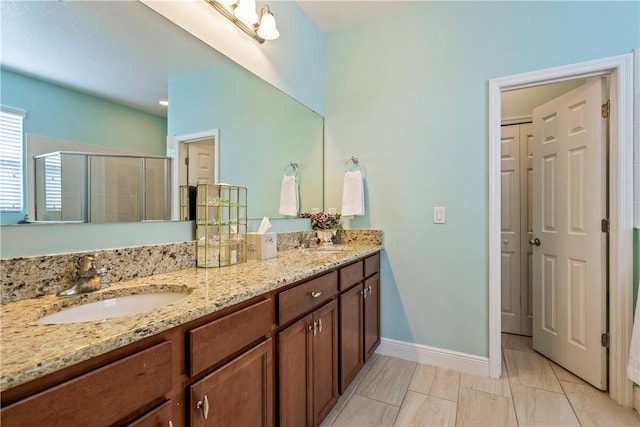 full bathroom with baseboards, a sink, double vanity, and a stall shower
