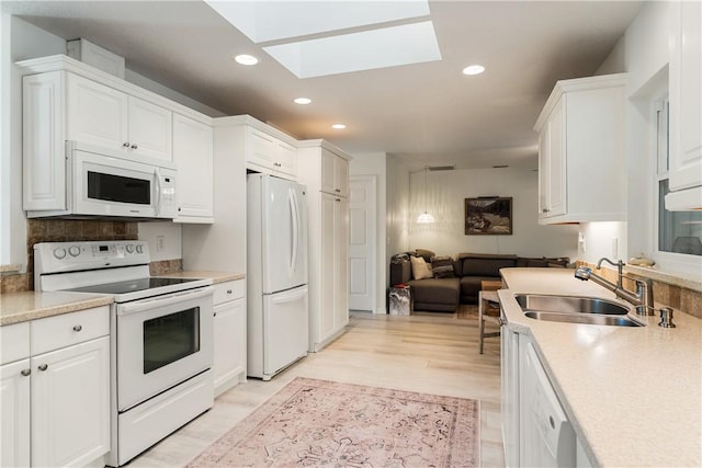 kitchen with a skylight, white appliances, sink, light hardwood / wood-style floors, and white cabinetry