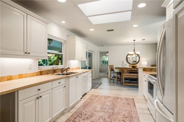 kitchen featuring pendant lighting, white appliances, white cabinets, a skylight, and plenty of natural light