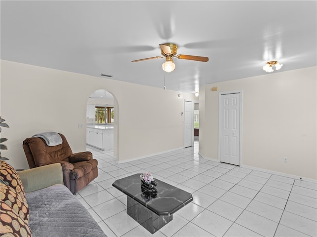 living area featuring light tile patterned floors, baseboards, arched walkways, and a ceiling fan