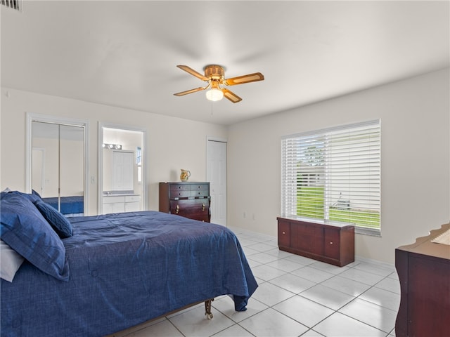 bedroom featuring light tile patterned floors, a ceiling fan, ensuite bathroom, and baseboards