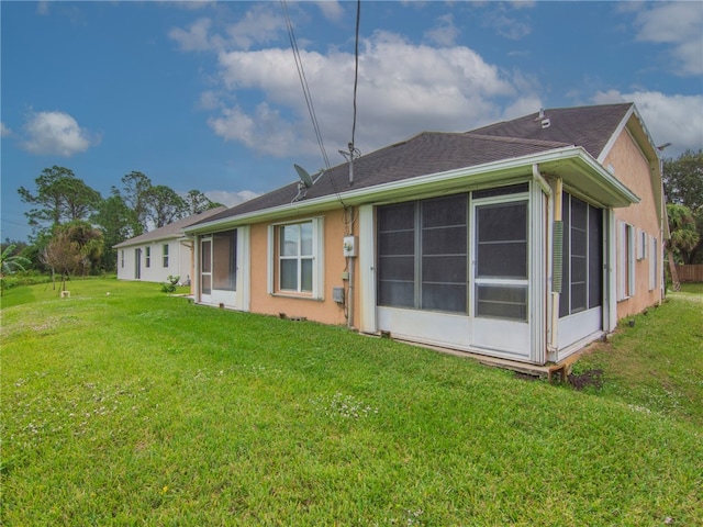 rear view of house featuring stucco siding, a lawn, roof with shingles, and a sunroom