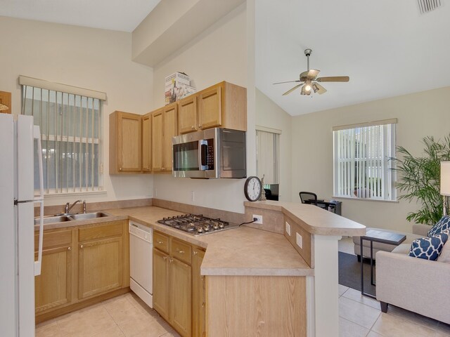 kitchen featuring appliances with stainless steel finishes, light tile patterned floors, light brown cabinetry, kitchen peninsula, and lofted ceiling