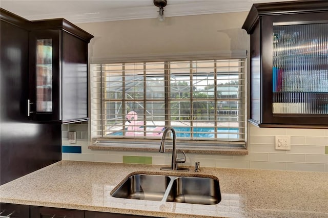 kitchen featuring sink, light stone counters, crown molding, decorative backsplash, and dark brown cabinets