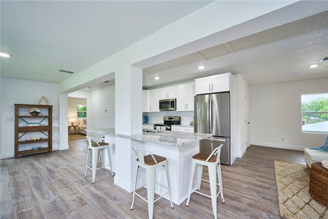 kitchen with a kitchen bar, white cabinetry, light stone counters, light wood-type flooring, and stainless steel appliances