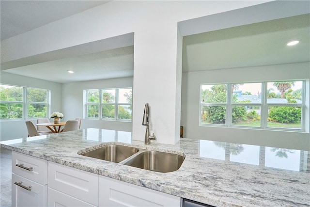 kitchen with light stone countertops, sink, and white cabinets