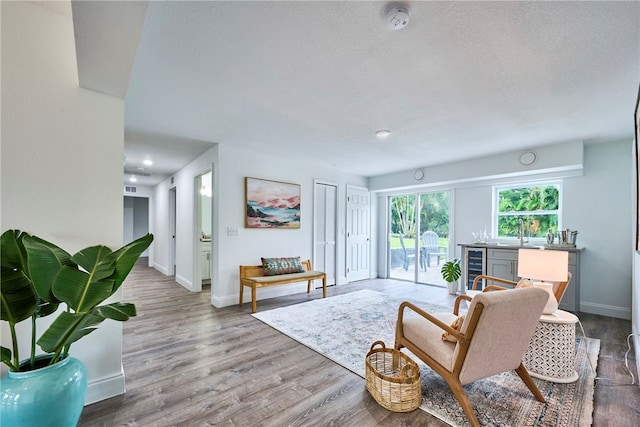 living room featuring a textured ceiling, bar, beverage cooler, and light wood-type flooring