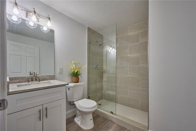 bathroom with toilet, a textured ceiling, a tile shower, vanity, and hardwood / wood-style floors