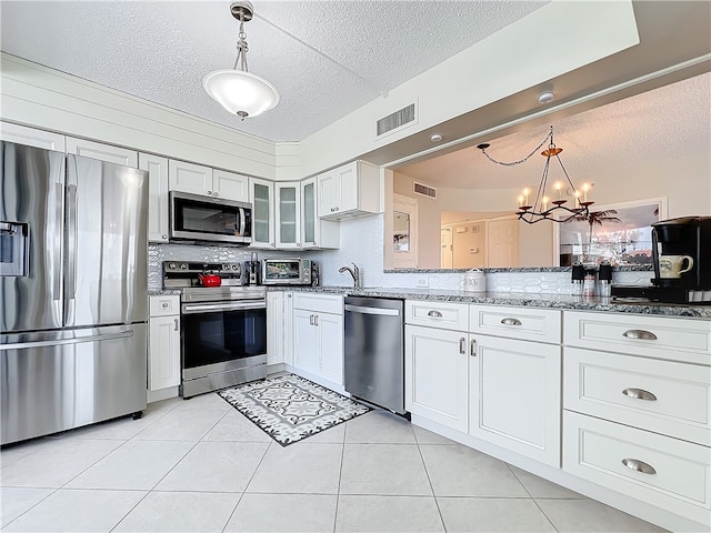 kitchen with a textured ceiling, white cabinets, decorative light fixtures, and stainless steel appliances