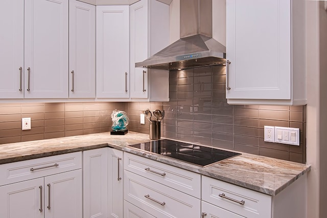 kitchen with black electric stovetop, backsplash, white cabinetry, and wall chimney range hood