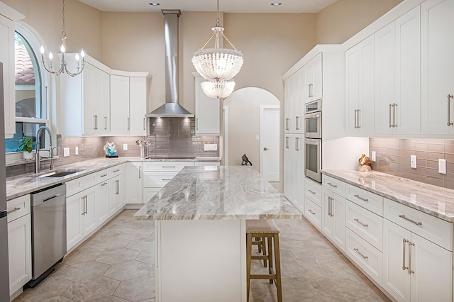 kitchen with appliances with stainless steel finishes, wall chimney range hood, sink, white cabinets, and a center island