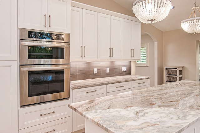 kitchen featuring tasteful backsplash, stainless steel double oven, pendant lighting, a chandelier, and white cabinetry