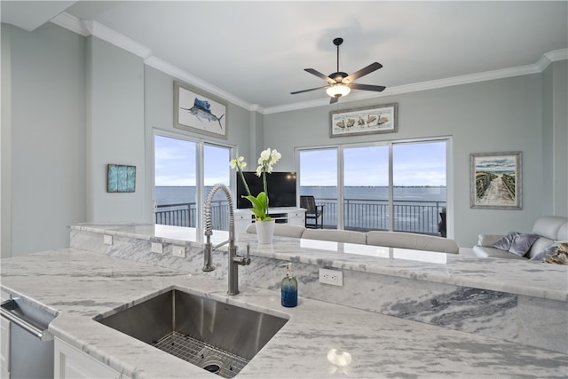 kitchen featuring light stone countertops, crown molding, open floor plan, and a sink