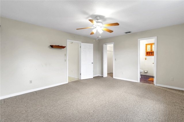 unfurnished bedroom with carpet flooring, a walk in closet, ensuite bathroom, and ceiling fan