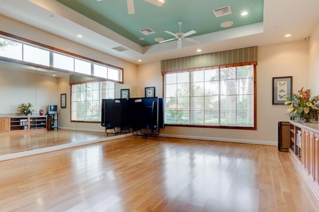 interior space featuring visible vents, a raised ceiling, a ceiling fan, and light wood finished floors