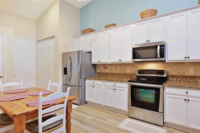 kitchen featuring light wood-style flooring, dark stone counters, stainless steel appliances, backsplash, and white cabinetry