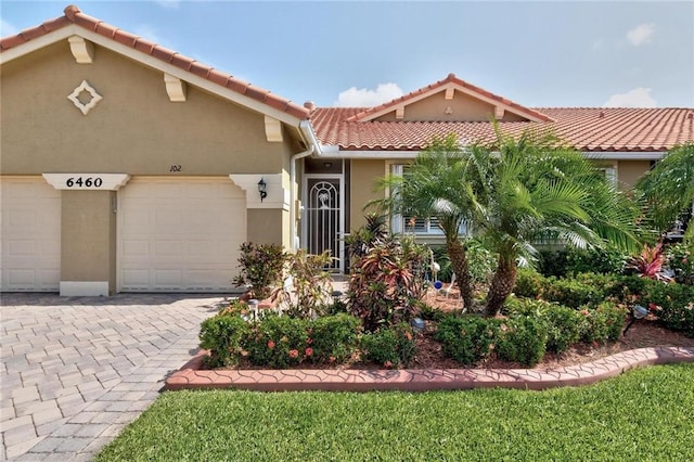 view of front of property featuring stucco siding, decorative driveway, a tiled roof, and a garage