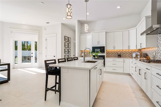 kitchen with sink, a kitchen breakfast bar, wall chimney exhaust hood, a kitchen island with sink, and pendant lighting