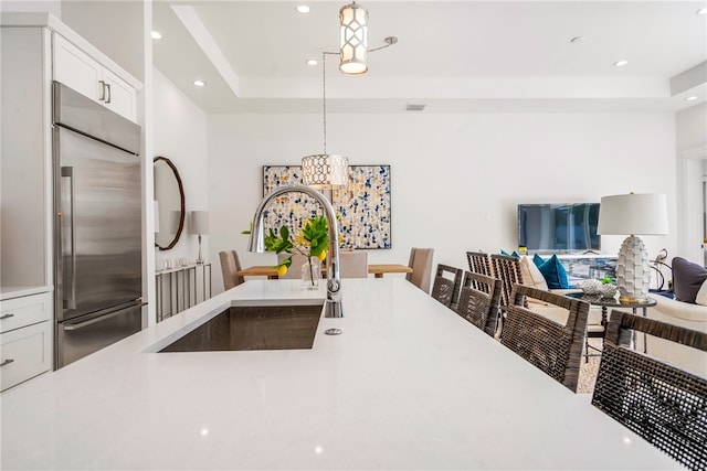 kitchen featuring pendant lighting, stainless steel built in refrigerator, sink, a tray ceiling, and white cabinetry