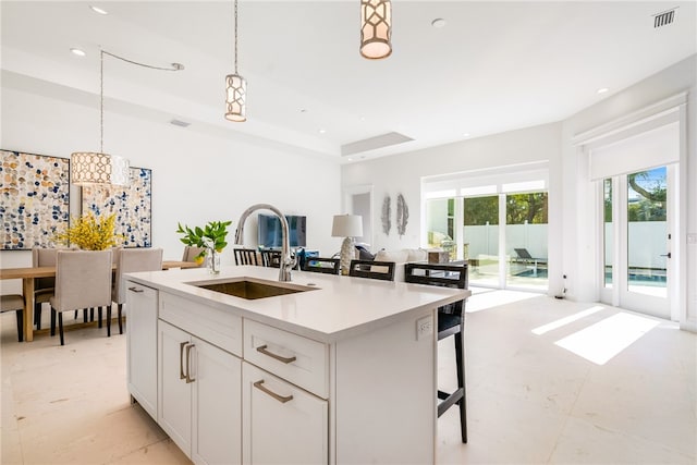 kitchen featuring decorative light fixtures, a kitchen bar, sink, an island with sink, and white cabinets