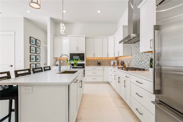 kitchen featuring a center island with sink, a breakfast bar area, wall chimney range hood, white cabinetry, and appliances with stainless steel finishes