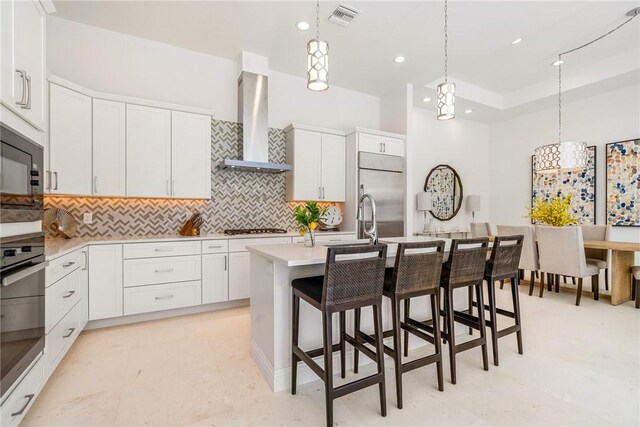 10 Strand Dr, Vero Beach, FL 32963 - kitchen with wall chimney exhaust hood, built in appliances, tasteful backsplash, hanging light fixtures, and light countertops
