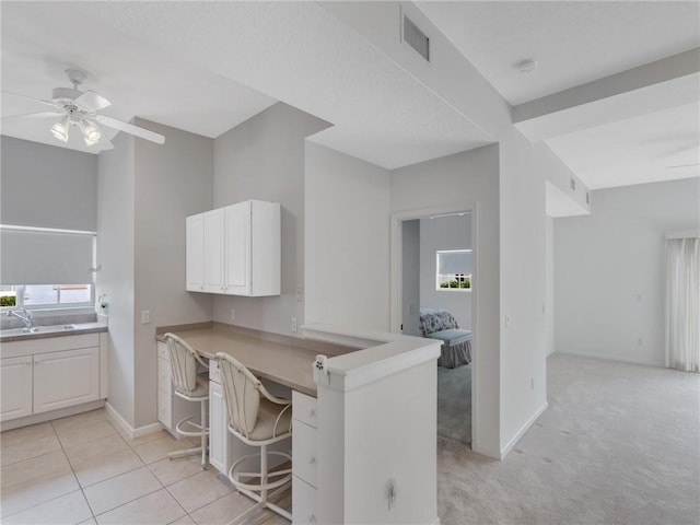 kitchen with a breakfast bar, kitchen peninsula, sink, ceiling fan, and white cabinetry