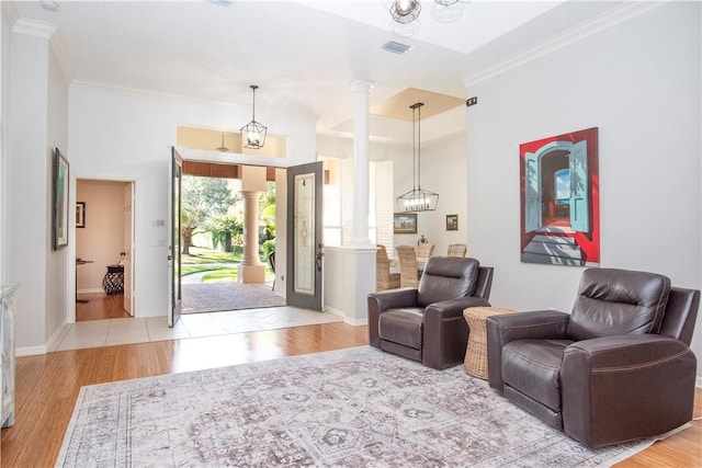 interior space featuring decorative columns, an inviting chandelier, ornamental molding, and light wood-type flooring