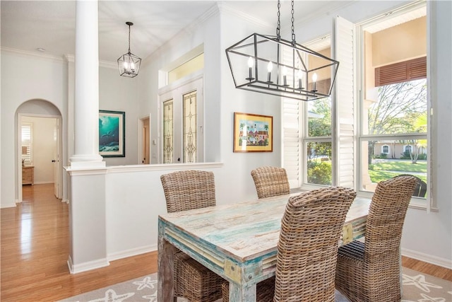 dining space with crown molding, light hardwood / wood-style flooring, decorative columns, and a chandelier