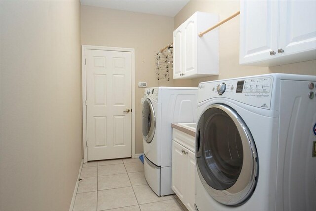 clothes washing area with light tile patterned flooring, cabinets, and washer and clothes dryer