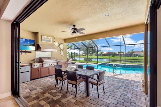 view of patio / terrace featuring glass enclosure, a water view, sink, area for grilling, and exterior kitchen