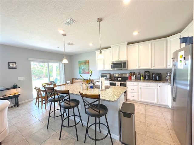 4173 Keeson Cir, Vero Beach, FL 32967 - kitchen with stainless steel appliances, light stone counters, white cabinets, an island with sink, and a breakfast bar area