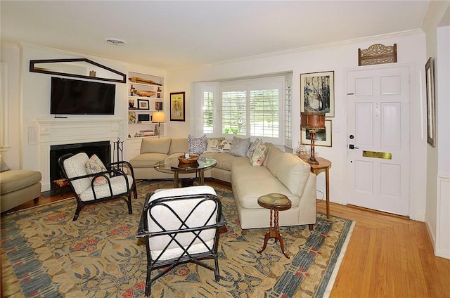 living room featuring crown molding, built in shelves, and light wood-type flooring