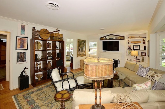 living room with built in shelves, wood-type flooring, a fireplace, and crown molding