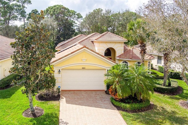 mediterranean / spanish home with stucco siding, a tile roof, decorative driveway, a front yard, and an attached garage