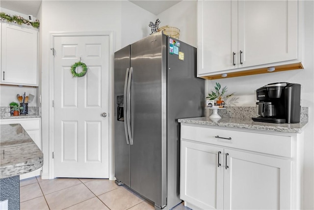 kitchen with white cabinets, light tile patterned flooring, light stone countertops, and stainless steel fridge