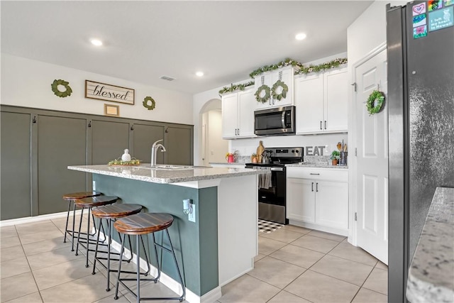 kitchen featuring light tile patterned floors, a breakfast bar area, white cabinetry, stainless steel appliances, and a center island with sink