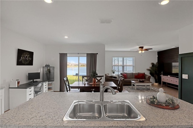 kitchen featuring sink, ceiling fan, light stone counters, an island with sink, and white cabinets