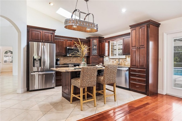 kitchen featuring a breakfast bar area, stainless steel appliances, light stone counters, decorative backsplash, and a kitchen island