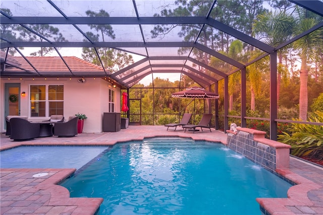 pool at dusk with a lanai, a patio, and pool water feature