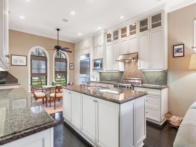 kitchen with built in appliances, dark stone countertops, dark hardwood / wood-style floors, a kitchen island with sink, and white cabinets