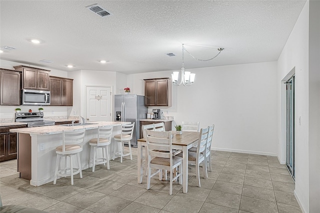 kitchen with an island with sink, sink, a notable chandelier, stainless steel appliances, and dark brown cabinets